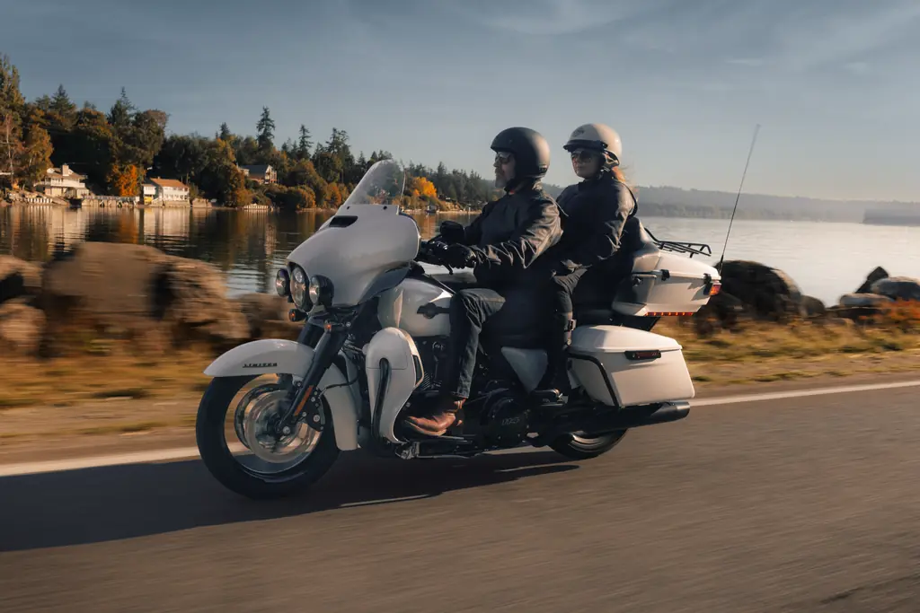 Harley-Davidson Ultra Limited 2024 blanche roulant en duo sur une route au bord d’un lac, avec Tour-Pak et bas de carénage visibles