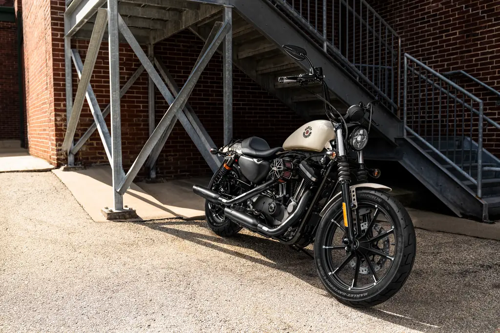 Une Harley-Davidson Iron 883 au réservoir crème, équipée d’accessoires d’origine et garée sous un escalier en fer