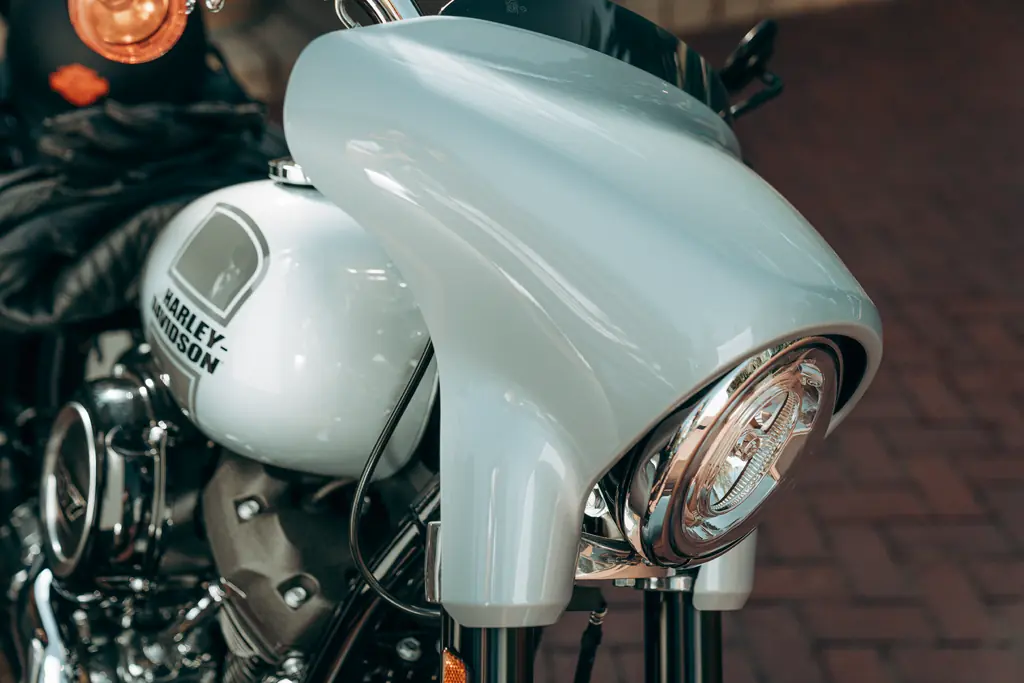 Gros plan du mini-carénage, du pare-brise court noir et du phare rond d’une Harley-Davidson Sport Glide FLSB de 2023.