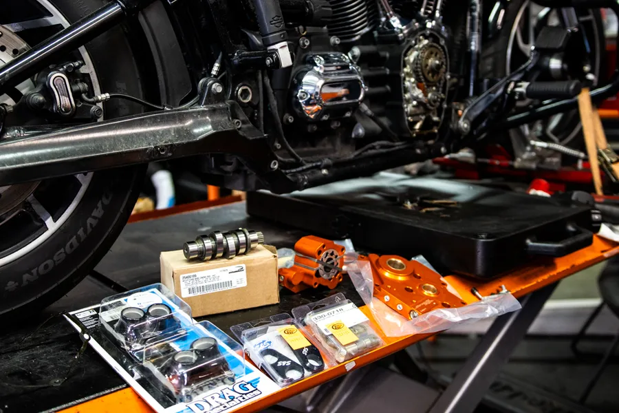Pièces Drag Specialties disposées sur un établi à côté d'un moteur Harley-Davidson sur pont élévateur